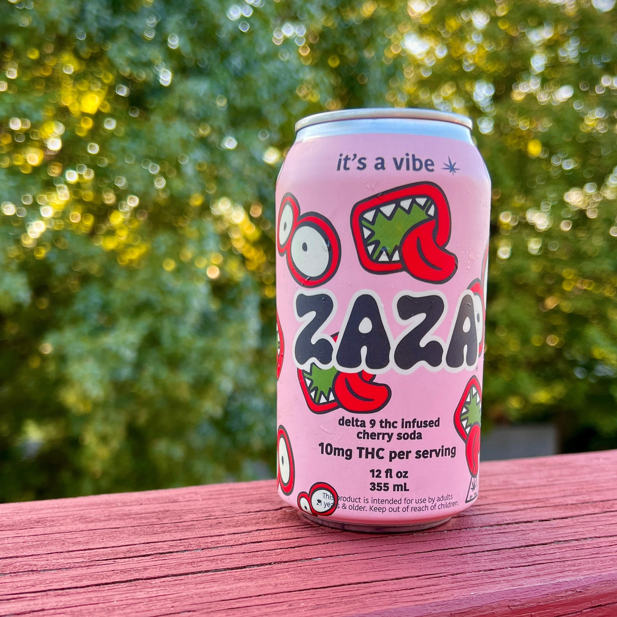Pink can with 'Zaza' branding on a wooden surface with greenery in the background